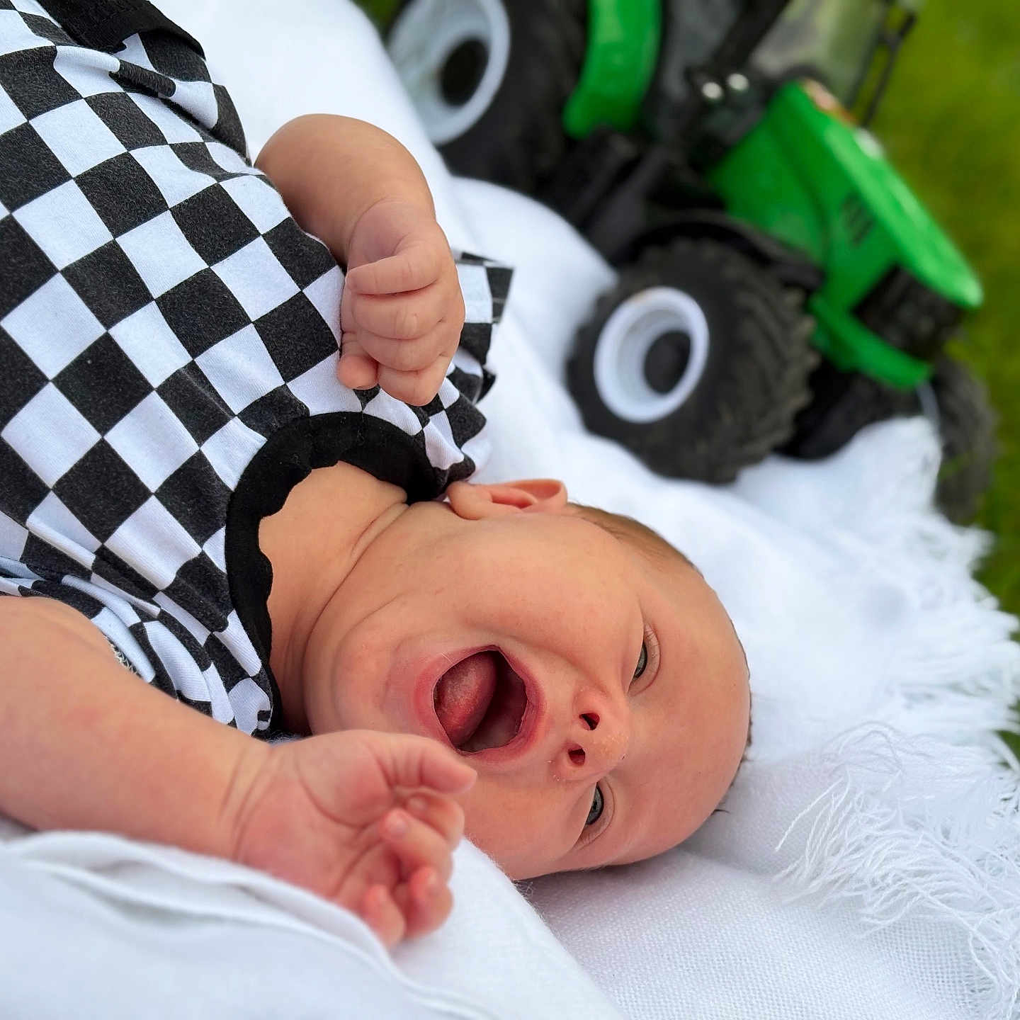 Riggins is registered to the contest to win money with this photo: baby, bodypart, clothing, face, finger, grass, hand, head, lawn, machine, newborn, person, photography, plant, portrait, spoke, t_shirt, transportation, vehicle, wheel
