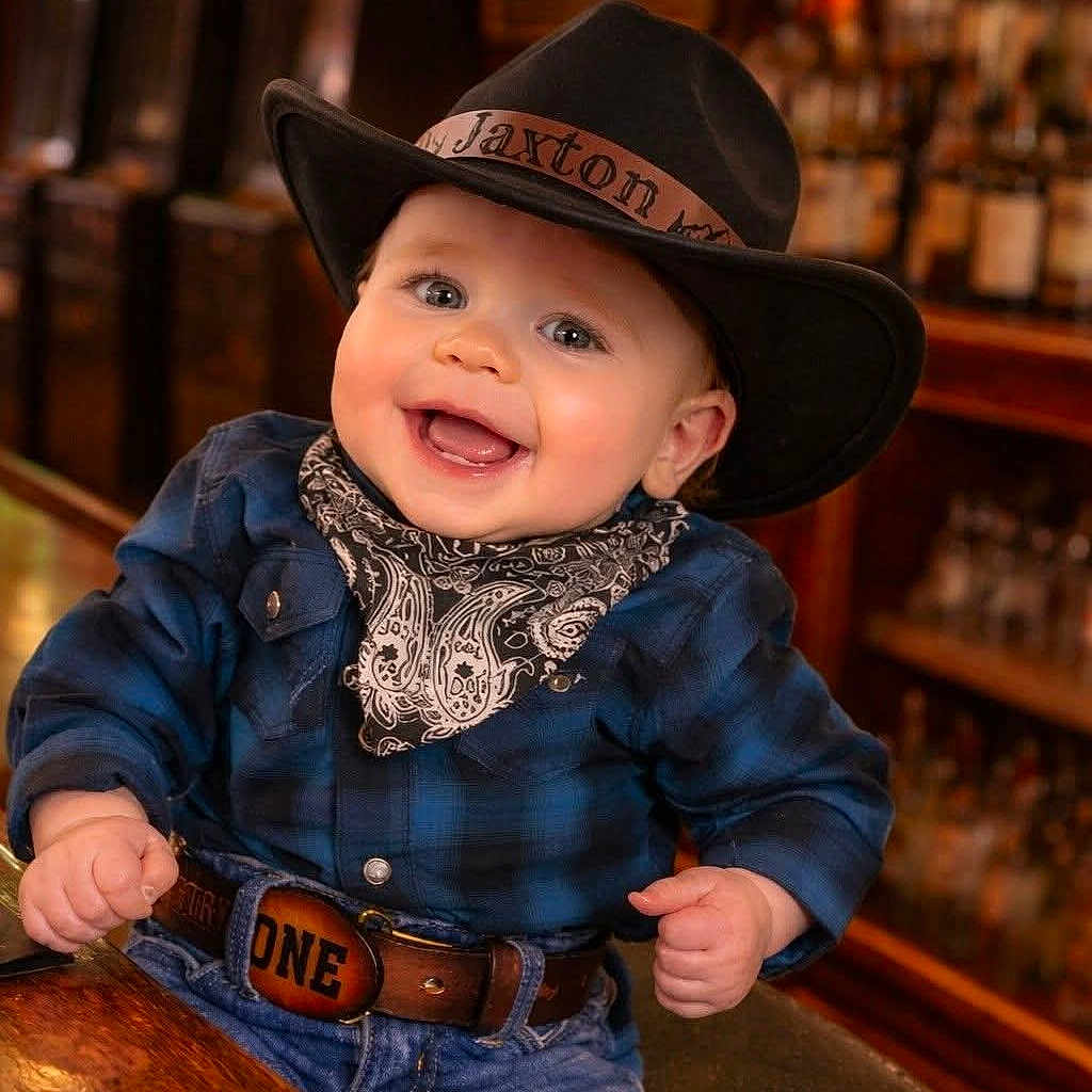 Jaxton joined the competition — help win amazing prizes! baby, child, cowboy, hat, bandana, belt, smiling, happy, portrait, indoor, jeans, plaid_shirt, cute, infant, western_style, person, clothing, face, closeup, celebration