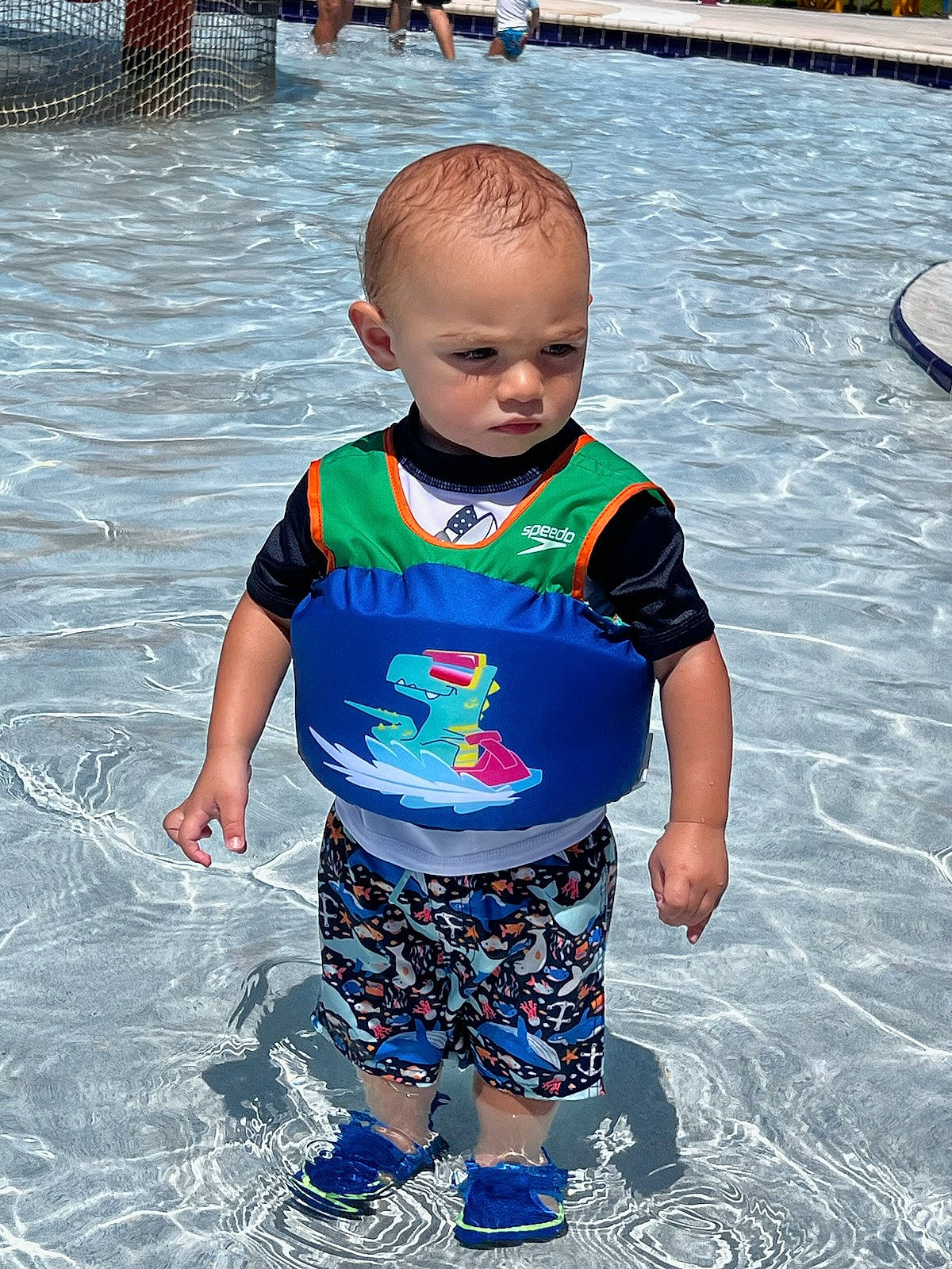 Aiden is registered to the contest to win money with this photo: body_of_water, cool, hairstyle, happy, human, leisure, mammal, people, person, photograph, product, recreation, sleeve, standing, summer, t_shirt, toddler, vertebrate, water, white