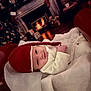 Remmie joined the competition — help win amazing prizes! baby, infant, red_hat, white_clothing, sleigh, christmas_tree, fireplace, holiday, festive, cozy, smile, indoors, warm_lighting, decorations, cute, blanket, wood_floor, portrait, child, seasonal