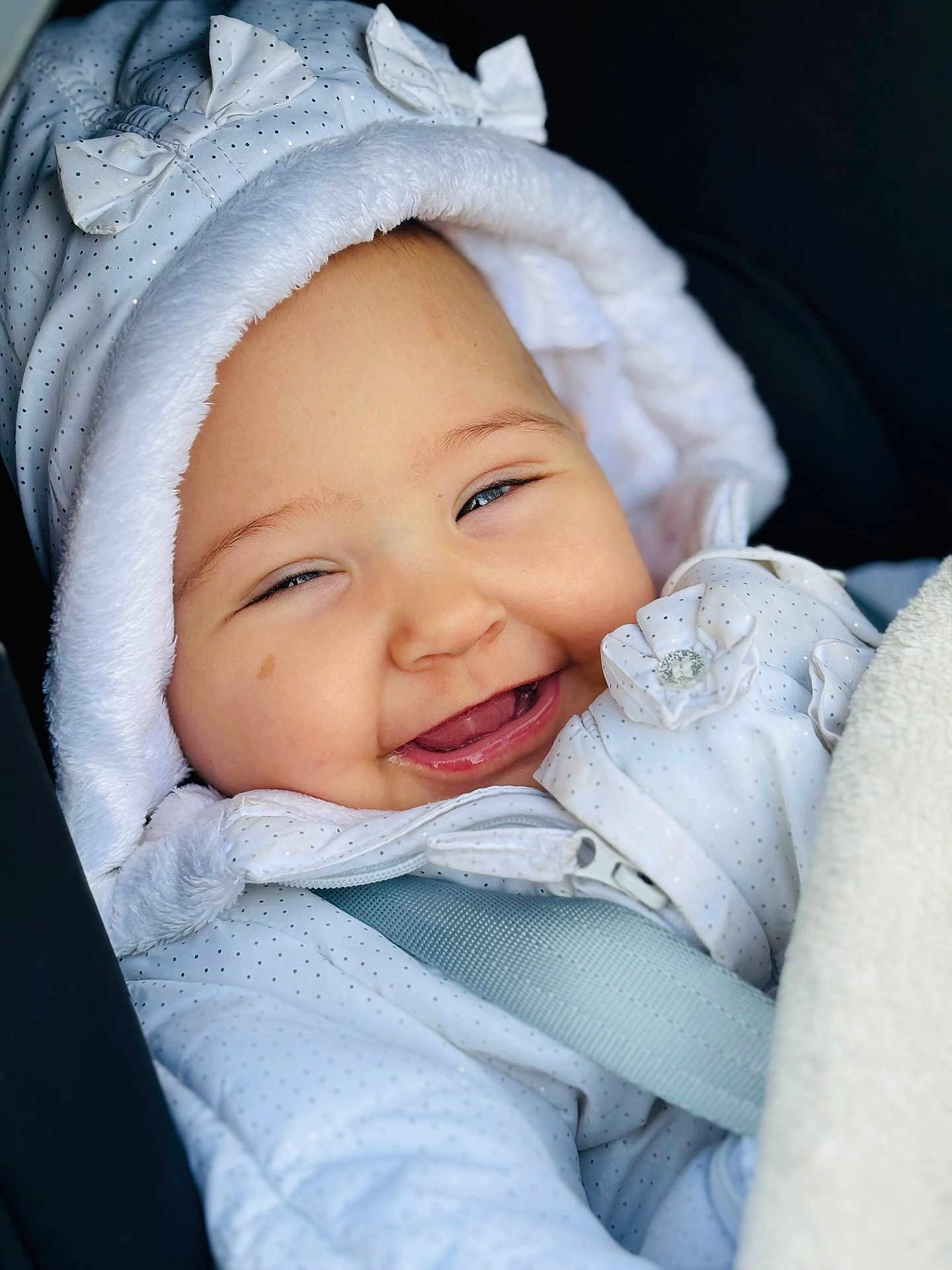 Naya participe au concours pour gagner de l'argent avec cette photo : baby, smiling, face, hood, jacket, polka_dot, bow, infant, cute, child, clothing, portrait, happy, closeup, warm, seatbelt, blanket, person, soft, cozy