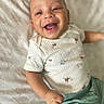 baby, child, infant, smiling, happy, laughing, portrait, close_up, lying_down, blanket, bed, clothing, onesie, green_pants, patterned_fabric, indoor, cozy, face, hand, photography