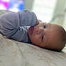 baby, infant, child, portrait, lying_down, bed, bedding, blue_clothing, long_sleeves, indoors, home, face, eyes, looking_at_camera, calm, cute, close_up, soft_lighting, blurred_background, photography