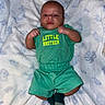 baby, infant, child, portrait, lying_down, blanket, green_outfit, shirt, shorts, socks, fists, face, eyes, smiling, indoor, bed, cozy, family, text_on_clothing, photography