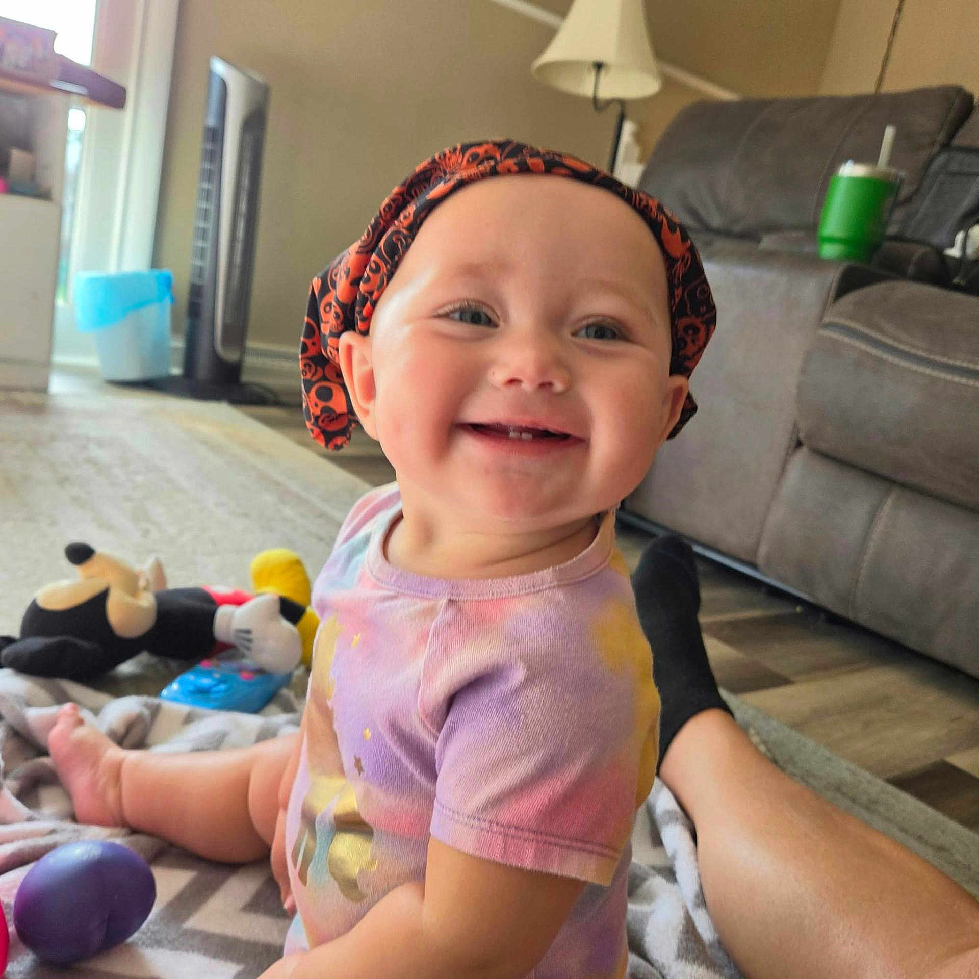 Charlotte is registered to the contest to win money with this photo: baby, child, infant, smiling, happy, portrait, bonnet, halloween, clothing, sitting, indoor, living_room, couch, lamp, toys, blanket, floor, playtime, family, photography