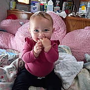 Charlotte is registered to the contest to win money with this photo: baby, child, infant, smiling, sitting, portrait, indoors, home, pink, blanket, pillow, couch, clothing, sweater, pants, socks, blue_eyes, hand, finger_nibbling, household_supplies