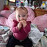 baby, child, infant, smiling, sitting, portrait, indoors, home, pink, blanket, pillow, couch, clothing, sweater, pants, socks, blue_eyes, hand, finger_nibbling, household_supplies