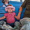 Charlotte is registered to the contest to win money with this photo: baby, child, infant, headphones, hearing_protection, pacifier, pink_clothing, floral_pattern, blue_bleachers, outdoor, stadium, seating, blanket, adult, family, portrait, sitting, looking_at_camera, playground, sports_venue