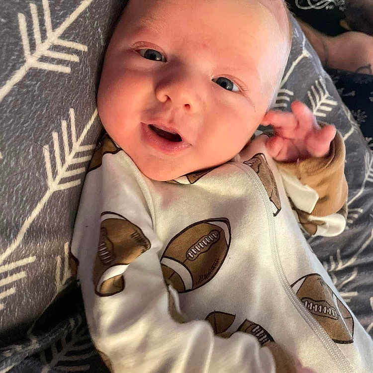 Aiden is registered to the contest to win money with this photo: baby, babylaughing, blanket, cushion, face, gun, happy, head, homedecor, newborn, person, photography, portrait, quilt, selfie, smile, weapon
