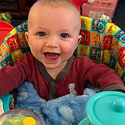 Leo is registered to the contest to win money with this photo: baby, infant, child, smiling, happy, portrait, sitting, activity_seat, toy, rattle, plush, blanket, colorful, indoors, playroom, nursery, chair, clothing, headshot, family_photo