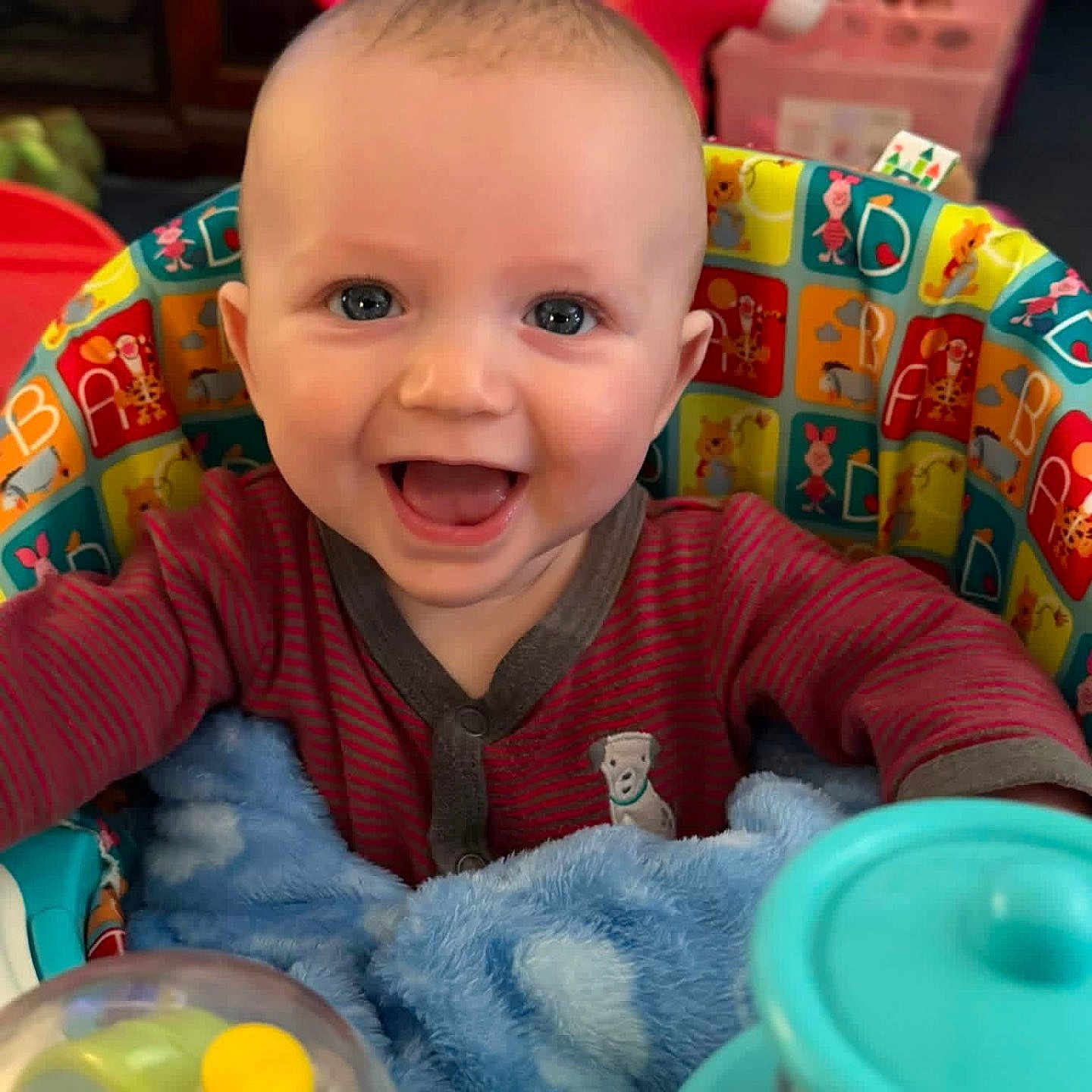 Leo is registered to the contest to win money with this photo: baby, infant, child, smiling, happy, portrait, sitting, activity_seat, toy, rattle, plush, blanket, colorful, indoors, playroom, nursery, chair, clothing, headshot, family_photo