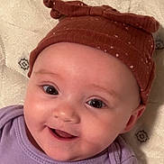 Alyza is registered to the contest to win money with this photo: baby, smiling, face, hat, brown_hat, purple_clothing, infant, cute, child, eyes, happy, portrait, close_up, headwear, baby_girl, soft_fabric, background, skin, cheeks, expression