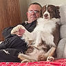 Uona participe au concours pour gagner de l'argent avec cette photo : australian_shepherd, blanket, blue_eyes, brown_and_white, couch, cozy, dog, fluffy, furniture, glasses, holding_paw, home, indoor, man, person, pet, portrait, red_blanket, relaxed, sitting
