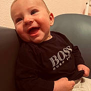 Elias a rejoint le concours — aidez-le/la à gagner de superbes lots ! baby, child, smiling, happy, portrait, face, clothing, black_shirt, text_on_clothing, sitting, chair, indoor, wall, cute, young, infant, skin, hand, head, eyes