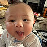 baby, infant, tongue_out, close_up, indoor, living_room, couch, cushions, furniture, person, cute, playful, child, home, carpet, blanket, wooden_cabinet, television, soft_lighting, smiling