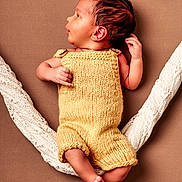 Kayden participe au concours pour gagner de l'argent avec cette photo : baby, infant, newborn, yellow_knitted_romper, soft_texture, white_knitted_fabric, brown_background, lying_down, floral_decoration, delicate_flowers, cute, small_feet, tiny_hands, portrait, studio_photo, warm_colors, cozy, peaceful, child, sleepy