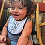 Micaden is registered to the contest to win money with this photo: baby, child, smiling, curly_hair, bib, blue_clothing, sitting, happy, closeup, face, skin, arm, foot, indoor, wooden_chair, blurred_background, portrait, cute, infant, natural_light