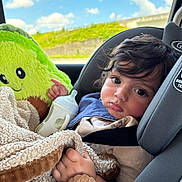 Micaden joined the competition — help win amazing prizes! child, toddler, car_seat, blanket, baby_bottle, plush_toy, avocado_toy, curly_hair, indoors, window, sky, clouds, greenery, seatbelt, clothing, portrait, expression, cute, baby, car_interior