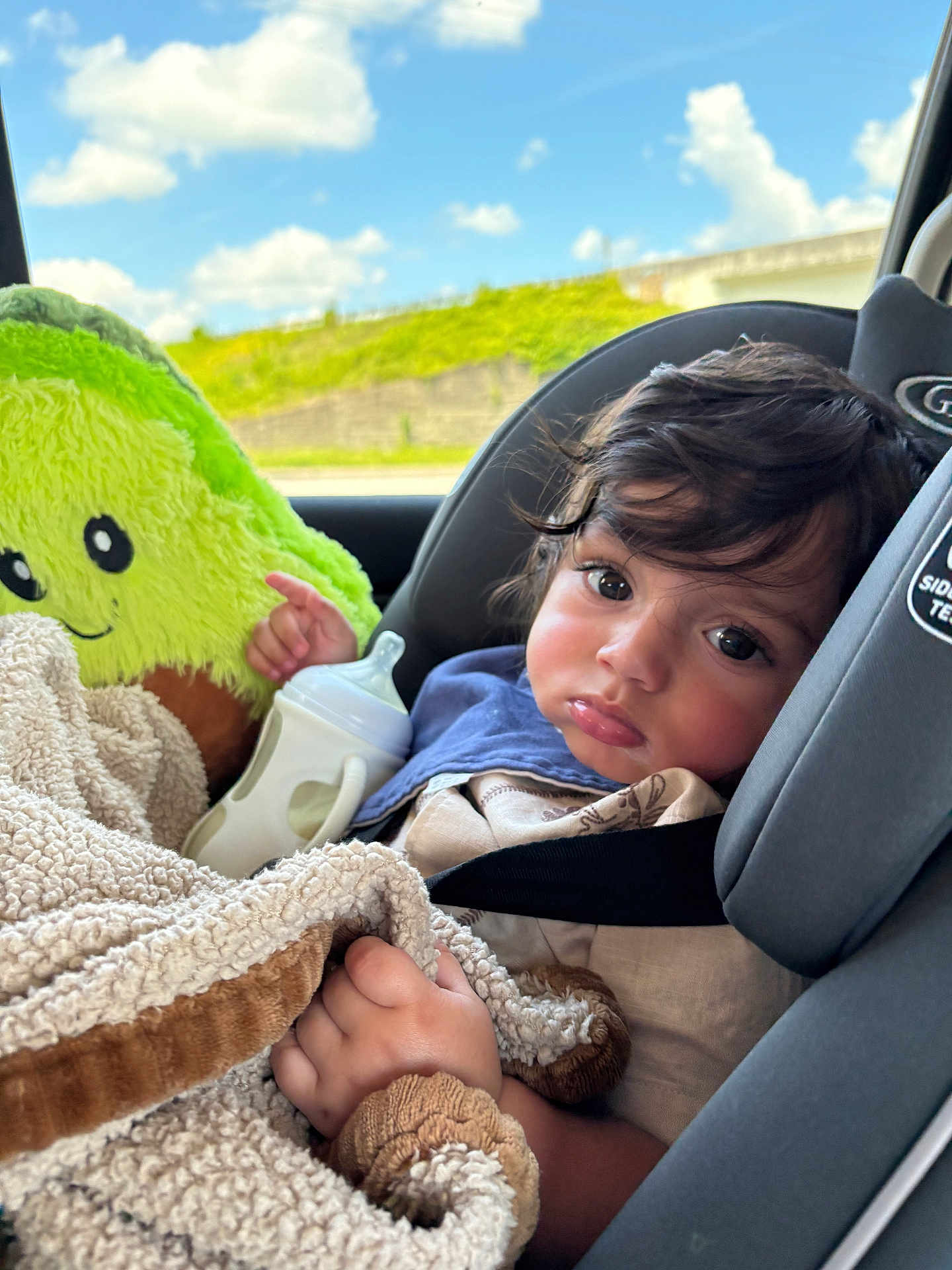Micaden joined the competition — help win amazing prizes! child, toddler, car_seat, blanket, baby_bottle, plush_toy, avocado_toy, curly_hair, indoors, window, sky, clouds, greenery, seatbelt, clothing, portrait, expression, cute, baby, car_interior