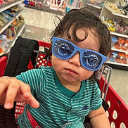 Micaden is registered to the contest to win money with this photo: toddler, child, shopping_cart, sunglasses, striped_shirt, toy, indoor, store, aisle, curly_hair, reaching_hand, red_cart, shopping, baby, retail, casual_clothing, cute, person, playful, fun