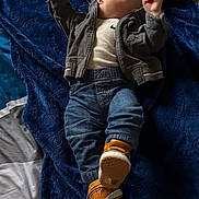 Aziel is registered to the contest to win money with this photo: baby, infant, child, lying_down, blanket, navy_blue, denim, jacket, shirt, jeans, sneakers, orange_shoes, fashion, portrait, indoors, bed, face, looking_up, raised_arms, safe