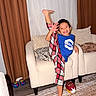 Darius joined the competition — help win amazing prizes! child, smiling, indoor, armchair, curtains, pillow, plaid_pants, blue_shirt, foot, carpet, football, happy, pose, home, furniture, person, living_room, barefoot, toy