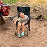 Darius is registered to the contest to win money with this photo: child, smile, outdoor, chair, dirt, grass, tshirt, footwear, picnic, bag, happy, person, nature, casual_clothing, sitting, playful, young, head_tilt, park, relaxation