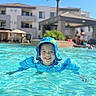 child, smiling, pool, water, floaties, hat, sun_hat, summer, outdoor, swimming, happy, blue, resort, palm_tree, vacation, sunny, leisure, kid, person, holiday