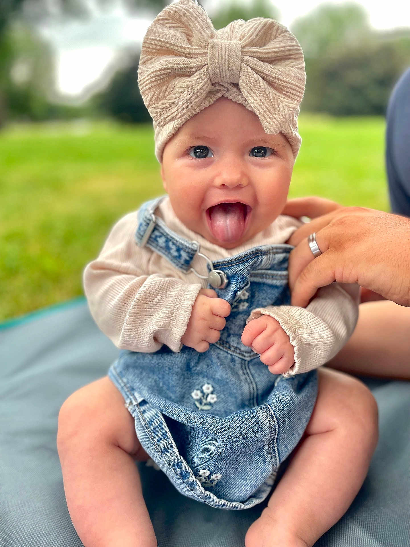 Giulia a rejoint le concours — aidez-le/la à gagner de superbes lots ! baby, child, tongue_out, headband, bow, denim_dress, sweater, hand, outdoor, grass, blanket, cute, smiling, happy, infant, person, portrait, sitting, nature, playful