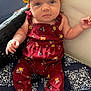 baby, child, infant, headband, yellow_headband, maroon_outfit, floral_pattern, cushion, blue_cushion, patterned_cushion, wicker_chair, indoor, seated, looking_up, cute, clothing, person, skin, hands, feet