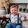 baby, child, smiling, plaid_shirt, suspenders, denim, blue_eyes, chair, cushion, knit_pillow, vase, pampas_grass, indoor, portrait, cute, happy, person, furniture, home, cozy