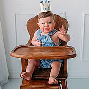Braxton joined the competition — help win amazing prizes! baby, child, high_chair, denim, overalls, crown, one_year_old, smiling, blue_eyes, wooden_furniture, indoor, minimalist, cute, happy, portrait, infant, sitting, playful, light, casual