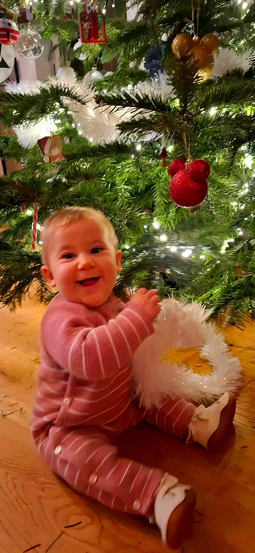 Agathe participe au concours pour gagner de l'argent avec cette photo : baby, celebration, cheerful, child, christmas_tree, cute, decorations, festive, garland, happy, holiday, indoors, infant, lights, ornaments, pink_onesie, seasonal, sitting, smiling, wooden_floor