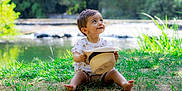 Léo participe au concours pour gagner de l'argent avec cette photo : barefoot, casual_clothing, child, cute, daytime, grass, greenery, happy, hat, nature, outdoor, playful, portrait, sitting, smile, summer, sunlight, toddler, water, young