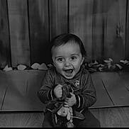 Léo a rejoint le concours — aidez-le/la à gagner de superbes lots ! background, black_and_white, child, clothing, cute, expression, face, floor, happy, indoor, joyful, person, playful, portrait, sitting, smiling, toddler, toy, wooden_floor, young_child