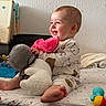 baby, child, smiling, pajamas, stuffed_animal, toy, bed, blanket, indoor, happy, person, foot, plush, colorful, cute, sitting, face, wall, cozy, home