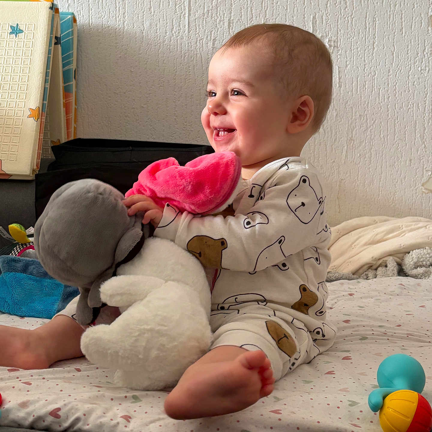 Mia participe au concours pour gagner de l'argent avec cette photo : baby, child, smiling, pajamas, stuffed_animal, toy, bed, blanket, indoor, happy, person, foot, plush, colorful, cute, sitting, face, wall, cozy, home