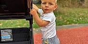 Loan a rejoint le concours — aidez-le/la à gagner de superbes lots ! toddler, child, barefoot, stroller, outdoor, playground, grass, greenery, shorts, white_shirt, blue_eyes, curious, summer, daylight, person, walking, standing, handle, wheel, park
