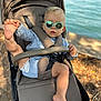 Loan participe au concours pour gagner de l'argent avec cette photo : toddler, stroller, sunglasses, child, outdoor, water, nature, sunlight, foot, hand, diaper, casual_clothing, seatbelt, shade, relaxing, summer, baby, portrait, playful, park