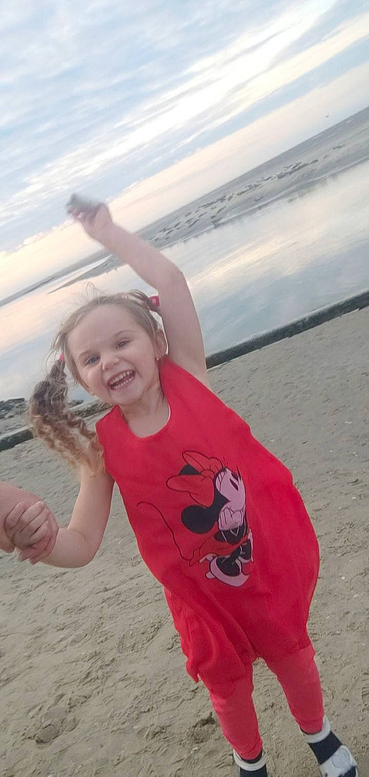 Joulia participe au concours pour gagner de l'argent avec cette photo : arm, beach, cloud, flash_photography, fun, gesture, happy, leisure, people_in_nature, people_on_beach, person, personal_protective_equipment, pink, recreation, shore, sky, smile, t_shirt, toddler, travel