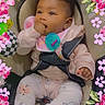 Imani is registered to the contest to win money with this photo: baby, infant, car_seat, pink_clothing, pacifier, bib, hand_in_mouth, floral_frame, cute, child, sitting, indoor, adorable, smiling, face, person, young_child, comfort, safe, decorative