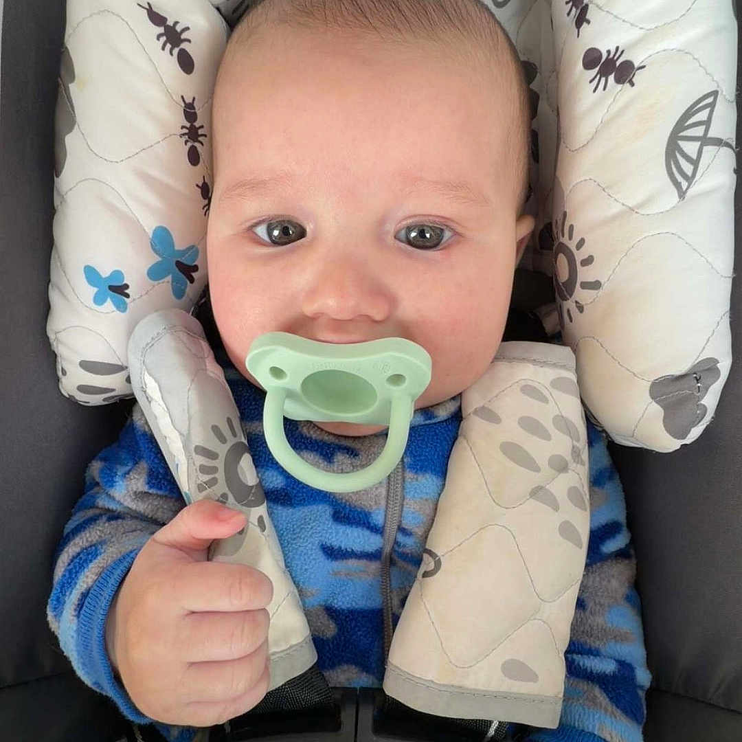 Roman joined the competition — help win amazing prizes! baby, pacifier, car_seat, blue_onesie, child, infant, face, hands, safety_harness, seat_belt, patterned_clothing, close_up, indoor, cute, portrait, head_support, comfort, young_child, infant_toddler, secure