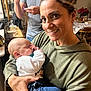 Cameron joined the competition — help win amazing prizes! baby, woman, person, indoor, holding, smile, sleeping, casual_clothing, man, family, table, chair, home, hoodie, jeans, hand, face, portrait, relaxed, cozy