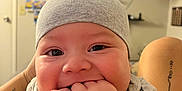 Kaisyn is registered to the contest to win money with this photo: baby, infant, cute, hat, gray_hat, indoor, cheerful, smiling, hands, fingers, tattoo, leg, television, blurred_background, person, child, closeup, face, happy, casual