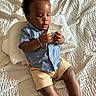 Juelz joined the competition — help win amazing prizes! toddler, child, baby, blue_shirt, beige_shorts, curly_hair, bracelet, sitting, bed, blanket, white_bedspread, packet, concentration, indoor, footwear, socks, cute, portrait, young_child, exploring