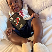 Juelz joined the competition — help win amazing prizes! baby, smile, phone, sneaker, sleeveless_sweater, slippers, couch, white_couch, happy, child, indoor, cute, portrait, person, hand, footwear, clothing, relaxing, infant, cozy