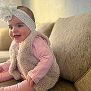 Seyanah participe au concours pour gagner de l'argent avec cette photo : baby, child, girl, headband, bow, pink_clothing, fuzzy_vest, sitting, couch, indoor, smiling, happy, cute, portrait, infant, person, cozy, soft_texture, bright_eyes, home