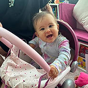 Anna participe au concours pour gagner de l'argent avec cette photo : baby, child, smiling, toy_stroller, indoor, person, hand, carpet, window, couch, toy, pink, white, clothing, face, happy, seat, childrens_toy, person_holding, living_room