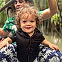 toddler, child, curly_hair, black_shirt, smiling, person, adult, hat, pants, elephant_pattern, outdoor, nature, greenery, portrait, happy, sitting, summer, casual_clothing, family, playful