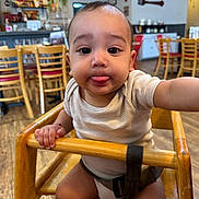 Ander is registered to the contest to win money with this photo: baby, child, high_chair, tongue_out, indoor, cafe, wooden_chair, person, cute, playful, infant, flooring, table, furniture, hand, face, clothing, seatbelt, expression, smile